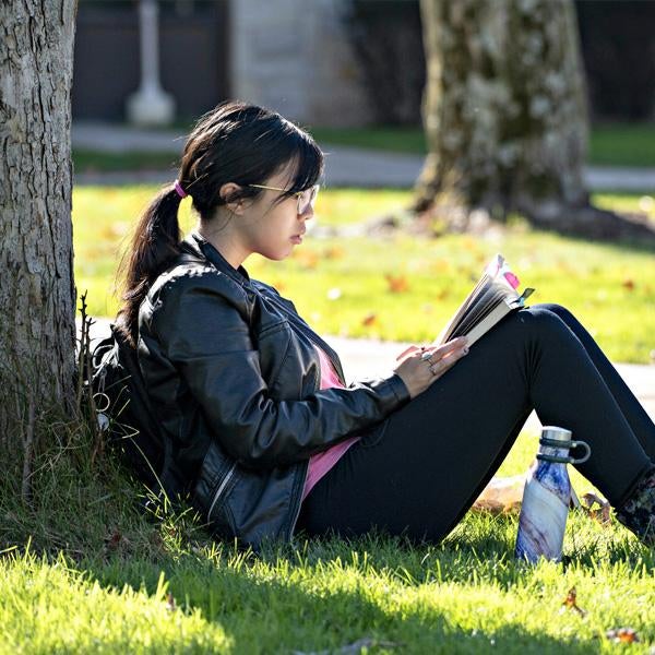 Student sitting against tree in grass