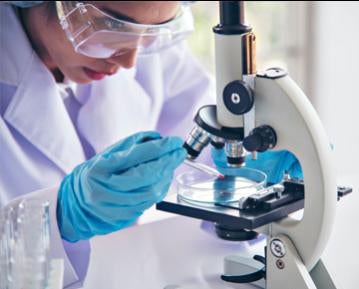 Person wearing lab coat and gloves using microscope