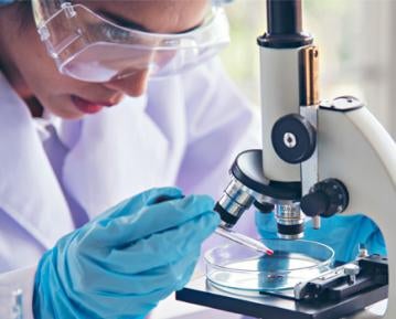 Person wearing lab coat and gloves using microscope